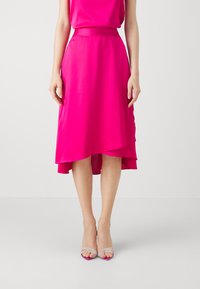 Magenta midi-skjørt med asymmetrisk hem, glatt tekstur og en tettsittende liv. Kombinert med gjennomsiktige hælsandaler.