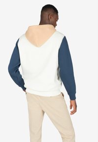 Sudadera con capucha que presenta un cuerpo blanco, mangas azul marino y una capucha beige. Textura suave con puños y dobladillo acanalados.
