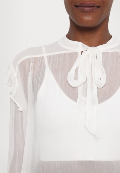 Witte doorschijnende blouse van een lichtgewicht, gestructureerde stof. Bevat een hoge nek, strikdetail en zachte gerimpelde mouwen.