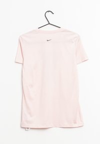 Jasnoróżowa koszulka Nike z krótkim rękawem, wykonana z gładkiej bawełny. Posiada małe czarne logo na górnej części pleców, zawieszona na czarnym haczyku.
