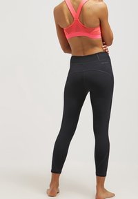Leggings neri con una fascia larga in vita e dettagli sulle cuciture, abbinati a un reggiseno sportivo rosa brillante con schiena a racer, che mette in risalto un design aderente.