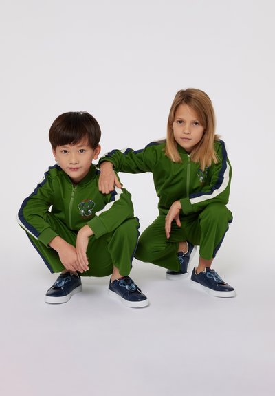 Tute sportive verdi con dettagli blu navy; giacca con zip completa e grafica di un elefante, pantaloni jogger abbinati e sneakers blu navy con design di elefante.