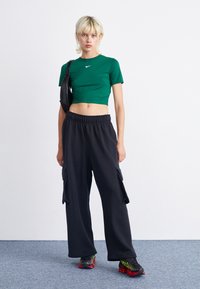 Vihreä lyhythihainen t-paita, jossa on Nike-logo, yhdistettynä löysiin mustiin cargo-housuihin, joissa on sivutaskut, sekä mustiin/punaisiin urheilukenkiin.