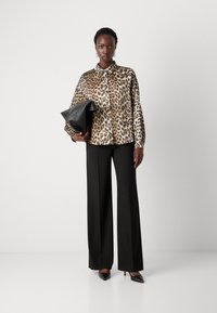 Løveprint knap-op skjorte i satin finish, båret med sorte vide bukser og sorte spidse hæle, mens der holdes en sort clutch.