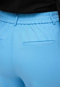 Lyseblå bukser med elastisk linning og glat tekstur, der har en stiklomme bagpå og et afslappet fit.