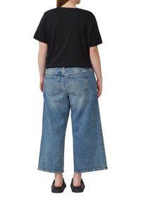 Zwart T-shirt met korte mouwen, gecombineerd met lichtblauwe, wijde jeans met twee achterzakken en een vervaagde denimlook. Zwarte instappers.