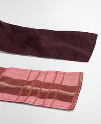 Twee stofstalen: de ene is een geribde donkerburgundy corduroy, en de andere is een roze ruitpatroon met bruine en groene accenten, met een gladde textuur.