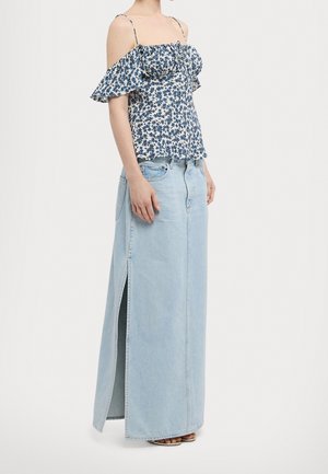 Vrouw draagt een blauw bloemenprint off-shoulder top met dunne bandjes en een lichtblauwe denim maxi rok met een split aan de zijkant.