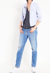 Světle modrá denimová bunda se stříbrnými knoflíky, námořnická květinová blůza, roztrhané světle modré džíny a bílé slip-on boty.
