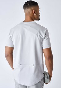 Camisa de manga corta gris claro con dobladillo curvo, que presenta detalles y costuras en negro, elaborada con una tela suave y texturizada.