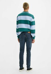 Felpa a righe verdi e blu con maniche lunghe, abbinata a jeans blu scuro. Sneakers nere completano l'outfit.