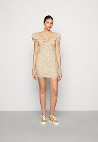 Vestido mini floral com mangas bufantes, apresentando um decote arredondado e uma silhueta ajustada em cores pastel. Usado com ténis amarelos.