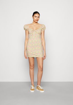 Vestido mini floral com mangas bufantes, apresentando um decote arredondado e uma silhueta ajustada em cores pastel. Usado com ténis amarelos.