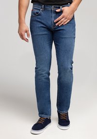 Dżinsy w średnim niebieskim kolorze, slim fit, z klasycznym pięciopocketowym wzorem i subtelnym szlifowaniem. W połączeniu z granatowymi sneakersami.