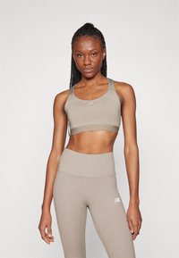 Soutien-gorge de sport beige avec bretelles réglables et détail de logo, associé à un legging beige taille haute avec des accents cousus et un logo.