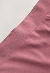 Gros plan d’un tissu rose poussiéreux avec deux motifs texturés distincts formant une section diagonale sur un fond clair.