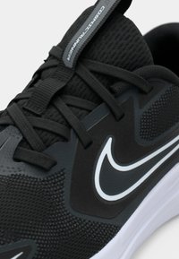 Close-up of black athletic shoe with textured fabric, black laces, white sole, and white Nike swoosh logo on side.