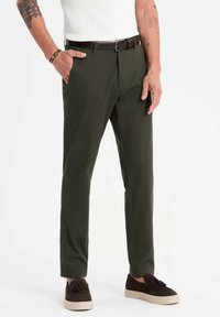 Olivgröna byxor, skräddarsydd passform, mjukt tyg, sidofickor, brunt läderbälte, bärs med bruna skor, enkel design.