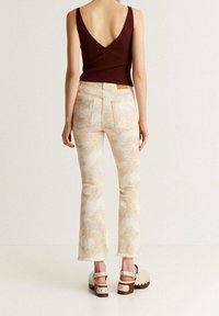 Top de tirantes de canalé marrón, jeans claros de corte acampanado con un patrón de tie-dye en tonos beiges y melocotón, y sandalias de plataforma blancas con acentos de tachuelas.