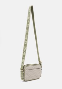 Grøn og beige crossover taske med et tekstureret stof, logo mønster, flad design og en mærketræk, der viser "KORS" i fed skrift.