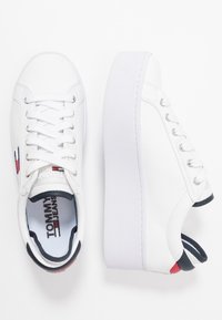 Baskets plateformes blanches en cuir lisse. Présentent un design à lacets, un bout rond et un logo de marque en contrastes de rouge, blanc et bleu.