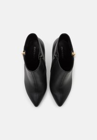Botas de cuero negro hasta el tobillo con punta afinada, que cuentan con un cierre lateral y acentos en dorado. Textura suave, diseño minimalista.