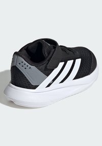 Scarpa sportiva nera con tomaia in mesh, design a tre strisce bianche, dettagli grigi sul tallone e suola bianca strutturata. Chiusura con cinturino regolabile.