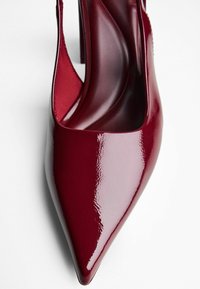 Glänzender, dunkelroter, spitzer High Heel mit Slingback-Riemen, von oben in Nahaufnahme auf einem weißen Hintergrund gezeigt.