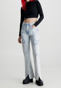 Pantalones cargo de color azul claro con bolsillos frontales, que presentan aberturas laterales y un diseño de pierna recta. Hechos de denim con un efecto de lavado desvanecido.