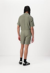 Romper verde de manga corta con canalé y cintura elástica. Presenta un cuello con solapas y se combina con zapatos y calcetas negras.