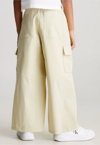 Ljusgula vida cargobyxor med bakfickor och sidfickor, tillverkade av andningsbart bomull. Kombinerade med vita sneakers.