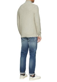 Hellgrauer gestrickter Pullover mit einem Rautenmuster, kombiniert mit blauen Jeans und weißen Sneakers, wobei die Bündchen und der Saum sichtbar sind.