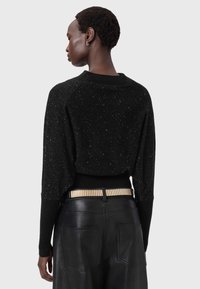 Schwarzer Pullover mit funkelnder Textur, im cropped Design und mit Raglanärmeln, kombiniert mit hochtaillierten Lederhosen und einem Gürtel mit goldenen Akzenten.