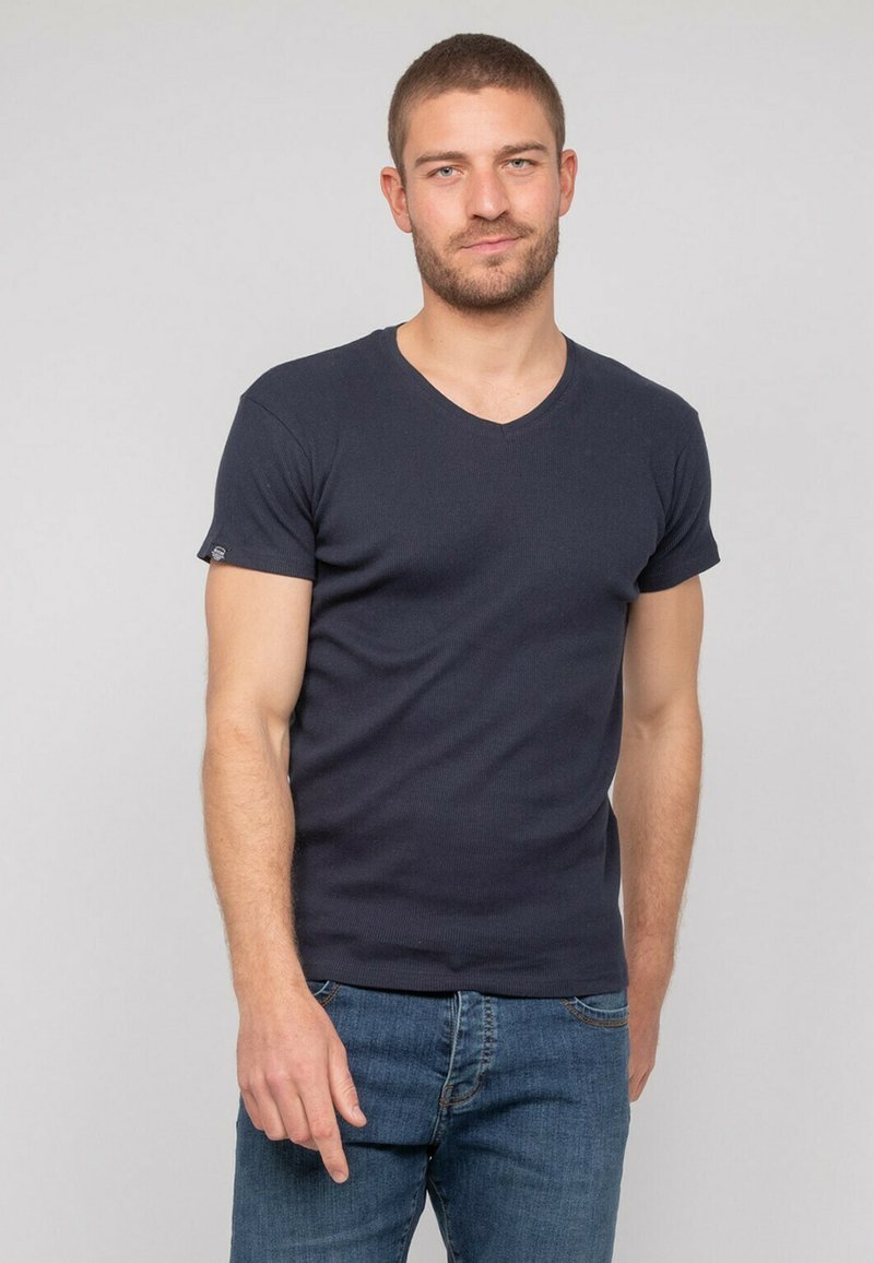 T-shirt à col V navy avec manches courtes, texture côtelée, design ajusté, associé à un jean en denim bleu. Pas de motifs ou de accents notables.