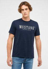 Granatowa bawełniana koszulka z krótkim rękawem i okrągłym dekoltem, z białym logo i napisem "MUSTANG" na piersi.