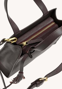 Sac à main en cuir marron foncé avec fermeture éclair dorée, sangle ajustable et détail de pompon sur fond clair.