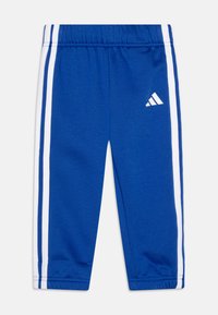 Pantalones deportivos azules hechos de tejido suave, con rayas laterales blancas y un logo bordado en la pierna izquierda. Cintura elástica.