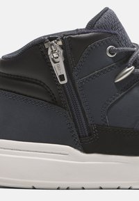 Höga sneakers i marinblå och svart läder, med en sidodragkedja, kontrasterande sömmar och en strukturerad mesh-överdel. Vit gummisula.