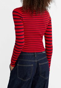 Rode geribbelde langdropped top met marineblauwe strepen, gecombineerd met donkerblauwe denim broek met vijf zakken en witte stiksels.