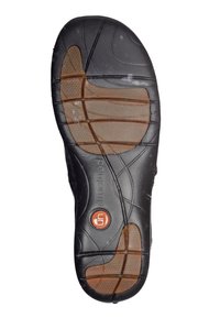 Schwarze Gummisohle mit strukturiertem Grip, braunen gemusterten Akzenten und einem runden Logo. Verfügt über tiefe Rillen für Traktion und Flexibilität.