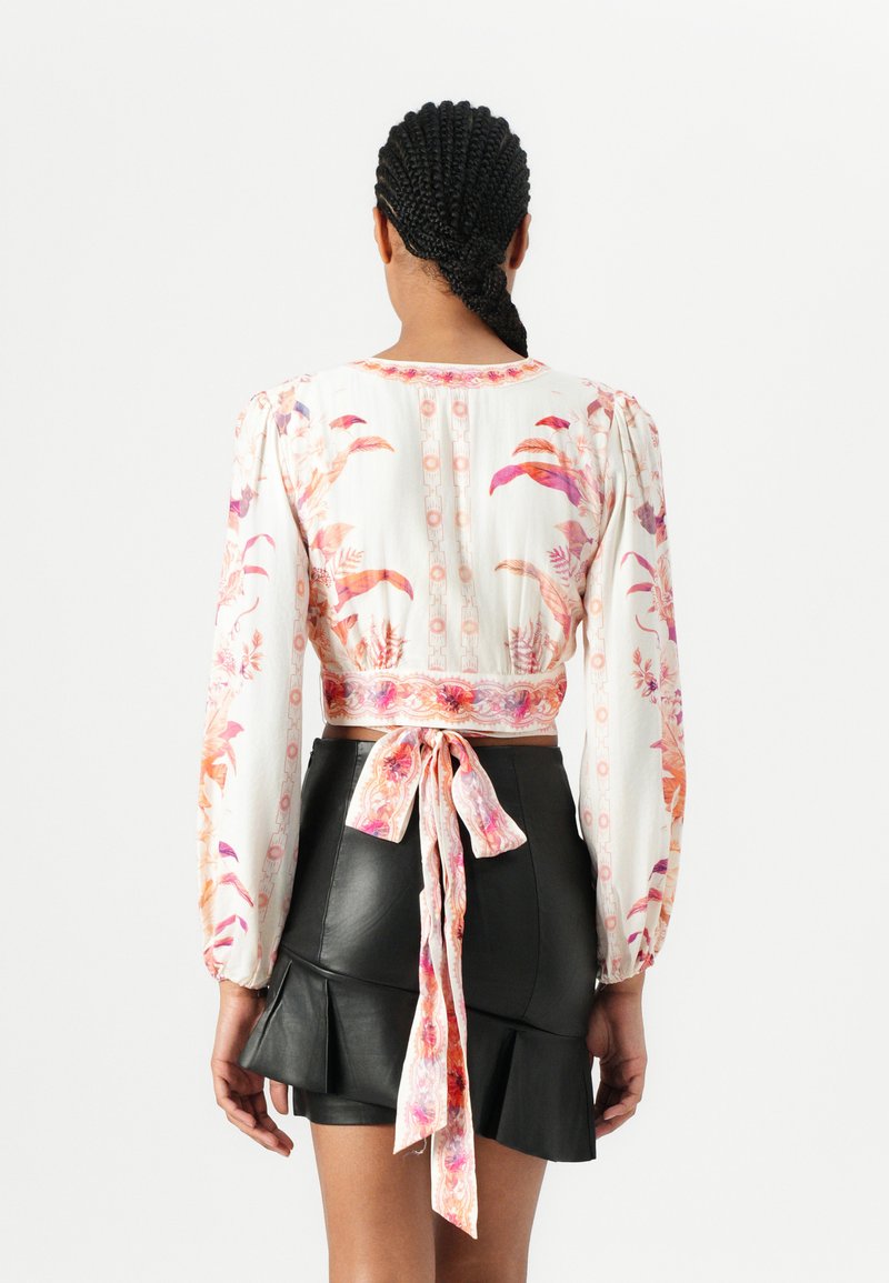 Weißes, blumiges Langarm-Crop-Top mit rosa und orangefarbenen Mustern, ausgestattet mit einem gebundenen Rücken, kombiniert mit einem schwarzen, ledernen, schwingenden Minirock.