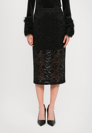 Woman wearing a black lace midi skirt with floral patterns, sheer lower half, paired with black high heels and a black top with fur sleeve cuffs.