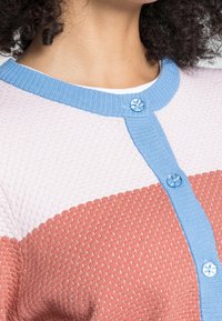 Knitted cardigan featuring a textured pattern in pink, coral, and blue. Button closure with a blue flower-shaped button accent.