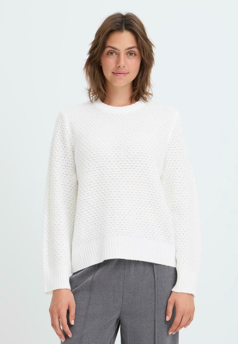 Weißer Strickpullover mit strukturiertem Muster, geripptem Ausschnitt und Ärmeln sowie einem kurzen Design. Kombiniert mit grauen Hosen.