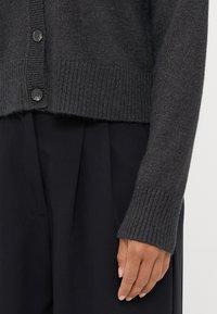 Mörkgrå ullkofta med ribbat avslut och ärmslut, prydd med runda svarta knappar framtill och med en avslappnad passform.