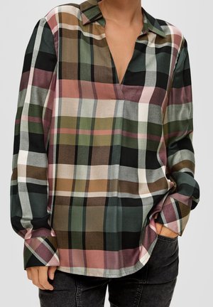 Chemise à manches longues à carreaux avec rayures vertes, roses, marron, noires et blanches, portée avec une main dans la poche, associée à un pantalon foncé.