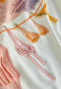 Delicate fabric embroidered with small beads outlining colorful lingerie pieces in pink, orange, and yellow on a white background.