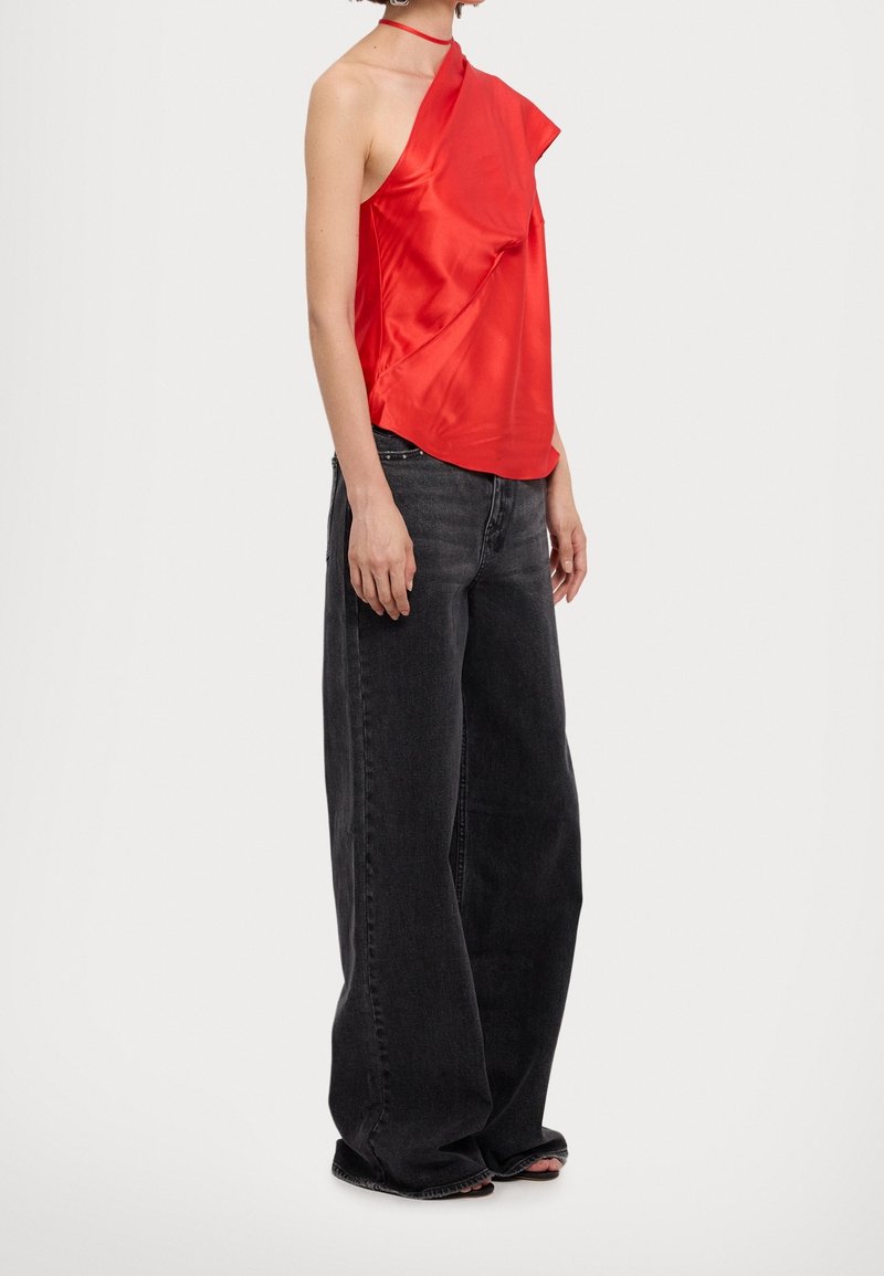 Haut rouge en satin à une épaule avec un design asymétrique, drapé, et une fine bretelle, associé à un jean en denim noir fluide.