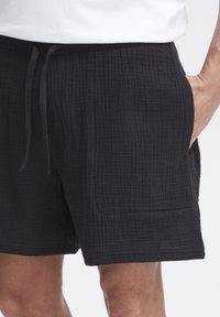 Bermudas negras y texturizadas, hechas de una tela ligera. Cuentan con una cintura elástica con cordón y bolsillos laterales. Diseño casual.