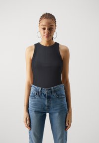 Svart ribbet tank topp med høy hals, kombinert med lyseblå høytaljede jeans. Stoffet ser mykt og tettsittende ut.